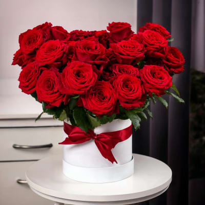 Red roses arranged in a white hat box with a red ribbon