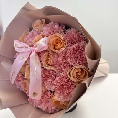 Pink bouquet of carnations and peach roses wrapped in blush paper
