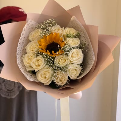 Hand-tied bouquet with a central sunflower surrounded by white roses in blush wrapping paper