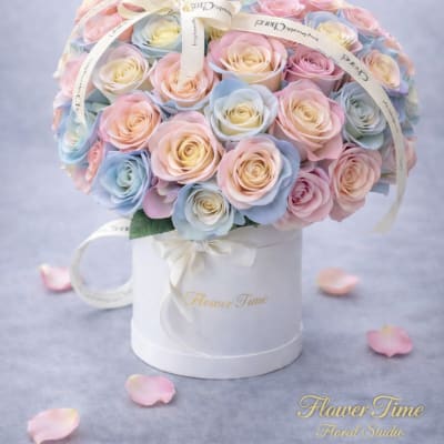 Pastel roses arranged in a white hatbox with ribbon.