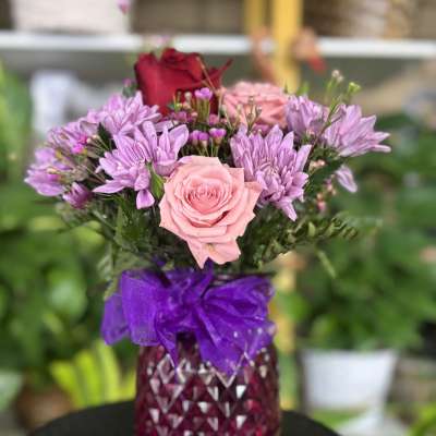 Pink and purple bouquet in a faceted magenta vase with a purple bow