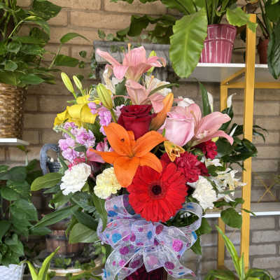 Colorful mixed flower arrangement in a tall pink vase with a decorative bow