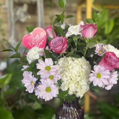 Pink roses and white hydrangea in a purple vase with daisies