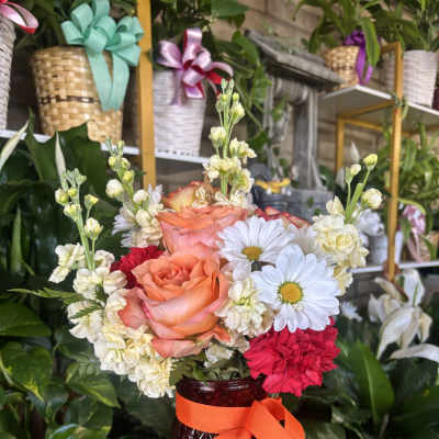 Peach roses and white daisies in a dark glass vase with an orange ribbon