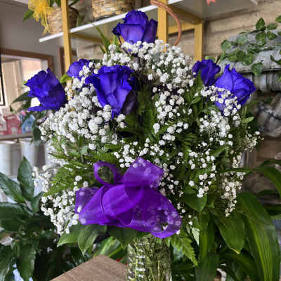 Clear vase of vivid purple roses with white filler flowers and a matching purple bow