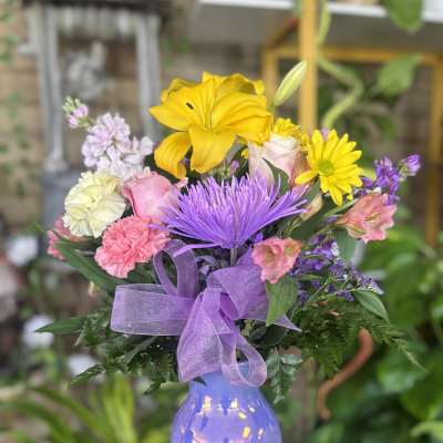 Mixed bouquet of yellow, purple, pink, and white flowers in a lavender vase