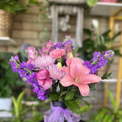 Pink and purple mixed bouquet in a dark vase with a lavender ribbon