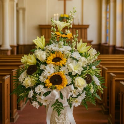 White and yellow floral arrangement in a church aisle with a ribboned vase
