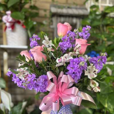 Pink roses and purple flowers in a patterned vase with a pink ribbon