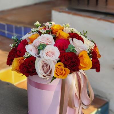 Round bouquet of red, pink, white, and yellow roses in a pink hat box