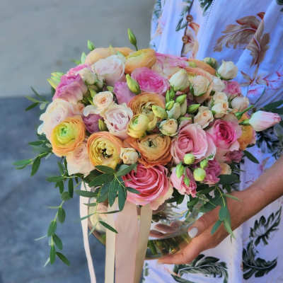 Handheld bouquet of pink, peach, and cream flowers with long ribbons