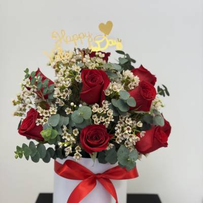 Red roses and white filler flowers in a white hat box with a red ribbon