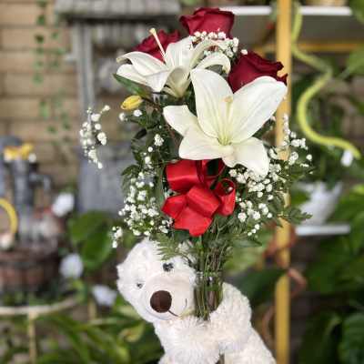 Bouquet of white lilies and red roses in a glass vase with a teddy bear