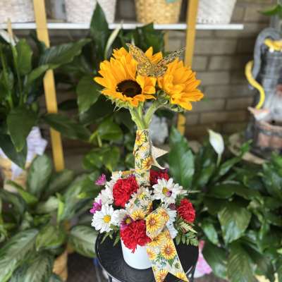 Sunflowers and mixed daisies in a white container with a decorative ribbon