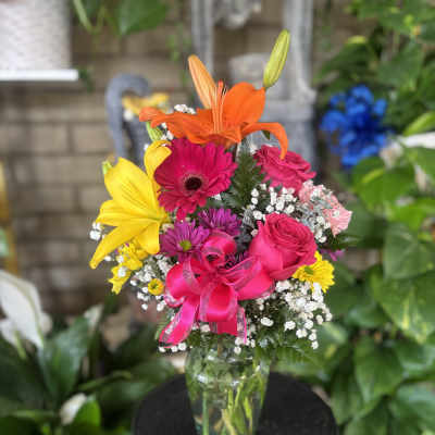 Bright mixed bouquet with lilies, roses, and a pink ribbon in a glass vase