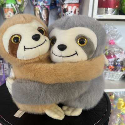 Two plush sloths hugging on a black display stand