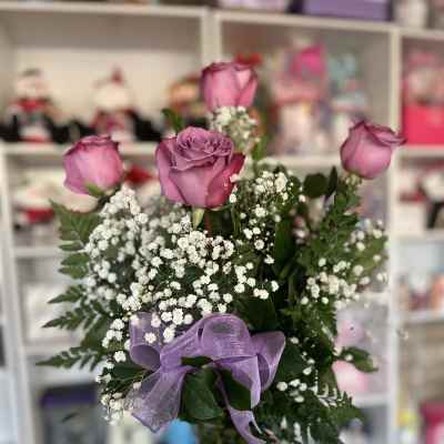 Pink roses in a glass vase with baby's breath and a purple ribbon