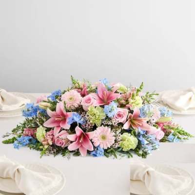 Low floral centerpiece with pink lilies, roses, and blue accents on a white table