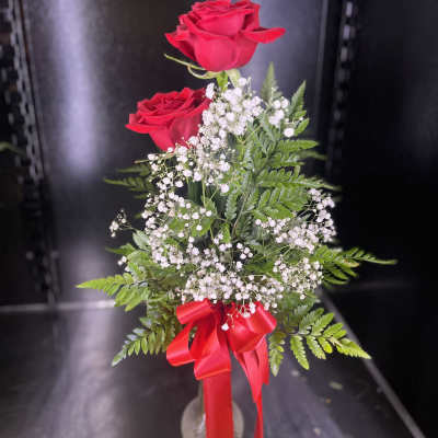 Two red roses with baby's breath in a clear vase and red ribbon