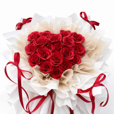 Heart-shaped bouquet of red roses wrapped in white and beige paper with red ribbons
