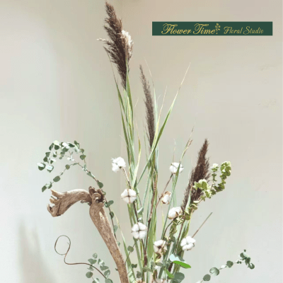 Tall dried floral arrangement in a patterned vase with cotton and pinecones