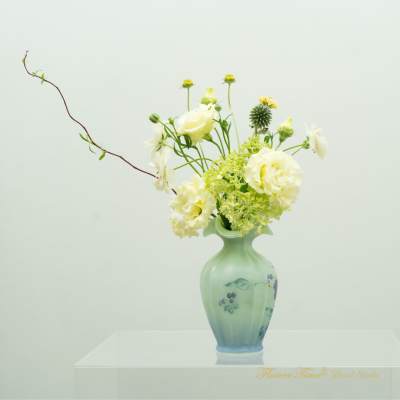 White flowers arranged in a green glass vase with a long branch accent