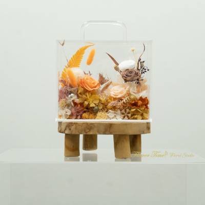 Clear box arrangement with orange and cream roses on a wooden stand