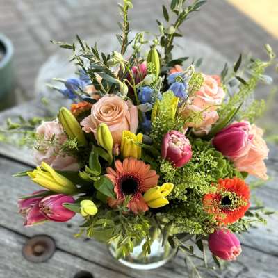 Mixed bouquet of roses, tulips, and gerbera daisies in a glass vase