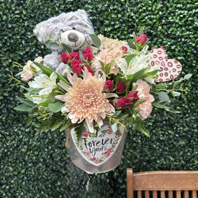 Bouquet with a teddy bear, pink roses, and pale flowers in a clear container