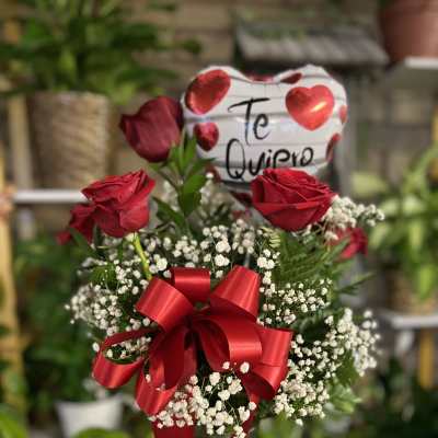 Red roses in a glass vase with baby’s breath and a heart balloon