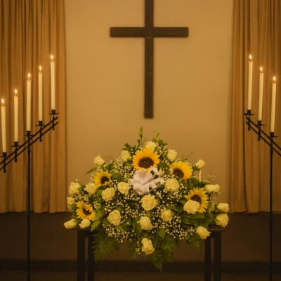 White rose and sunflower funeral arrangement in a church with candles and a cross