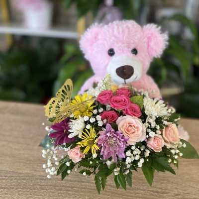 Pink teddy bear behind a mixed bouquet of roses and daisies