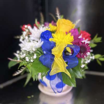 Colorful bouquet in a white vase with blue and yellow ribbon