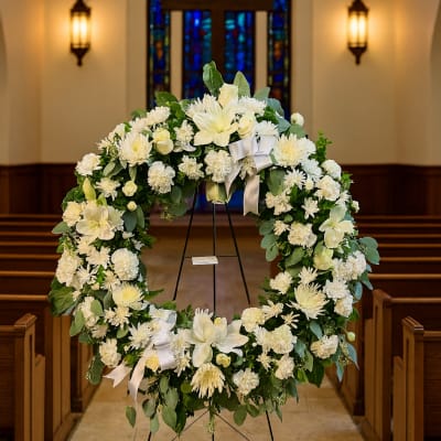 Large white floral wreath on a stand in a church aisle