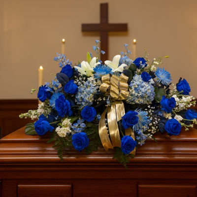 Blue and white floral spray on a casket with a gold ribbon
