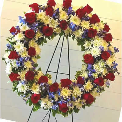 Large floral wreath of red roses, white blooms, and blue flowers on a stand