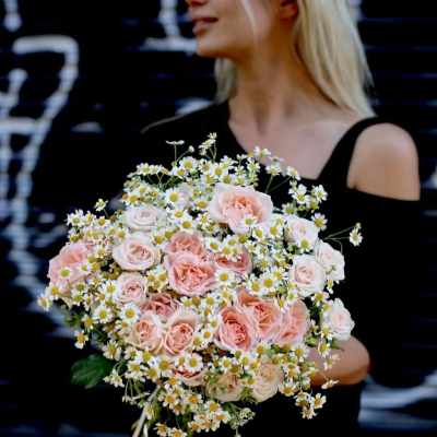 Woman holding a bouquet of pale pink roses and small white daisies
