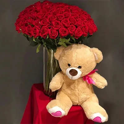 Red rose bouquet with a teddy bear sitting beside it