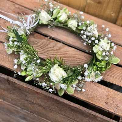 White floral wreath with small blossoms and ribbon on a wooden surface