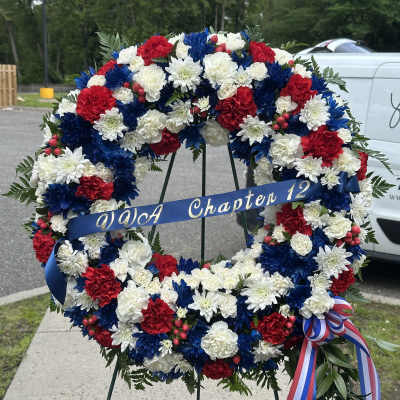 Red, white, and blue floral wreath on a stand with a ribbon