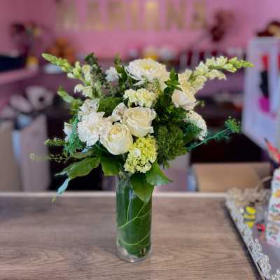 White roses and mixed white flowers arranged in a tall glass vase