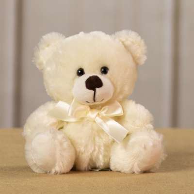Cream teddy bear with a satin bow sitting on a tan surface