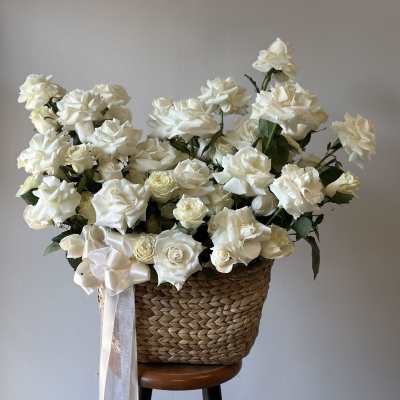 White roses arranged in a woven basket with a satin ribbon
