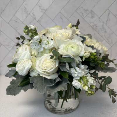White roses and ranunculus in a clear glass vase with gray-green foliage