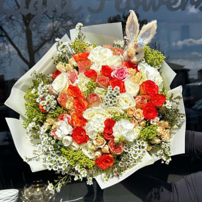 Large bouquet of red, white, and peach roses with a small bunny topper