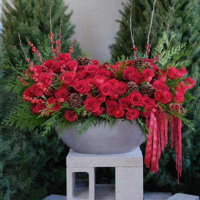 Red rose arrangement in a gray bowl with pinecones and berries