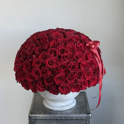 Large dome arrangement of red roses in a white pedestal vase with a red ribbon