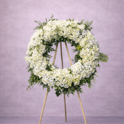 Large white floral wreath displayed on a wooden easel against a soft lavender background