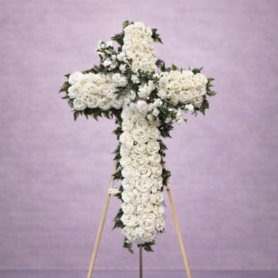 Standing cross-shaped spray of white roses on a wooden easel against a soft lavender background