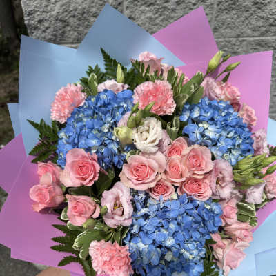 Bouquet of blue hydrangeas, pink roses, and carnations wrapped in pastel paper